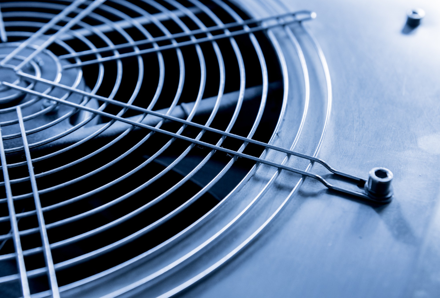 Close-up of a metal ventilation fan grille with a blue-toned metallic surface in the background.