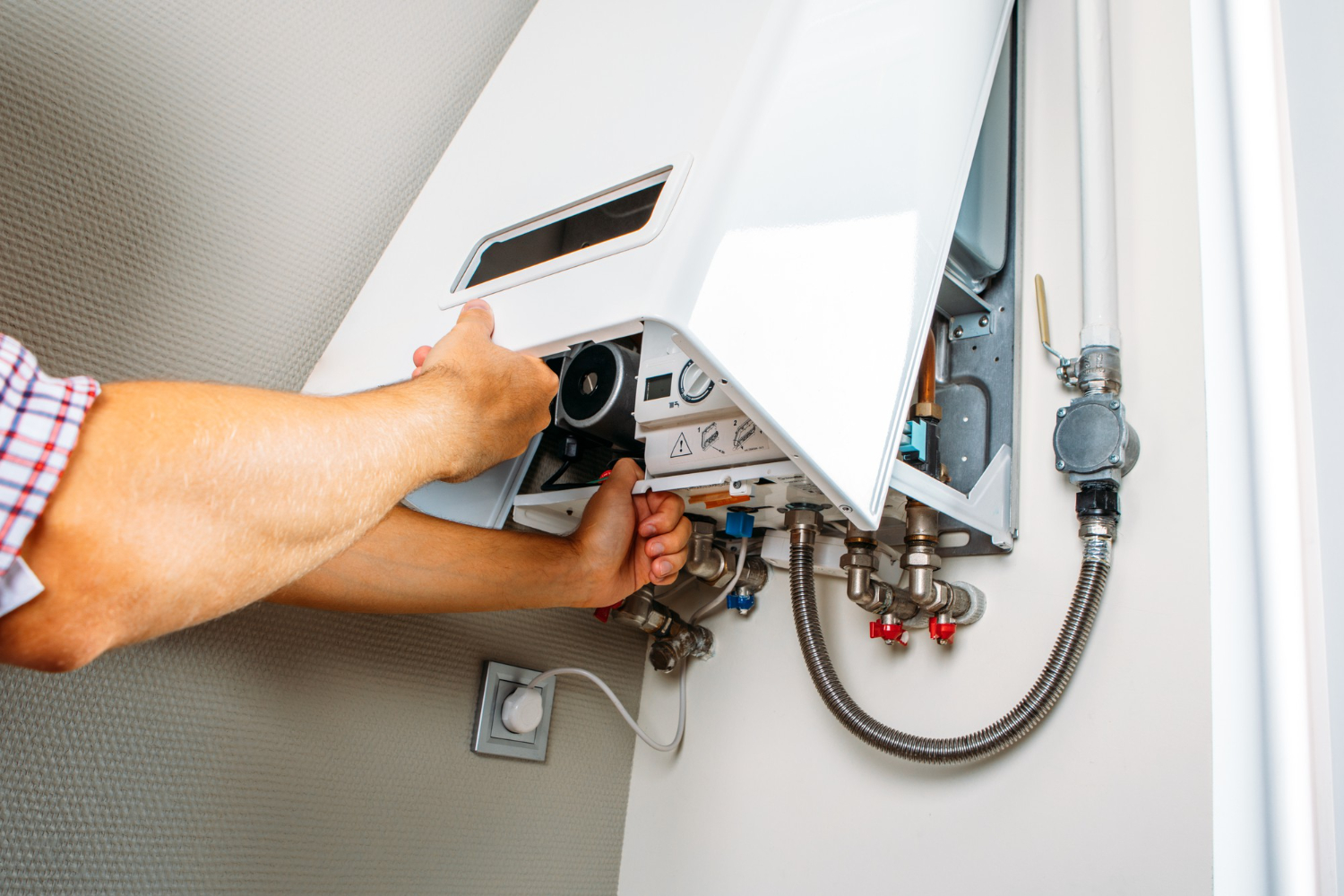 Person repairing or inspecting a wall-mounted gas boiler with tools and exposed components visible.