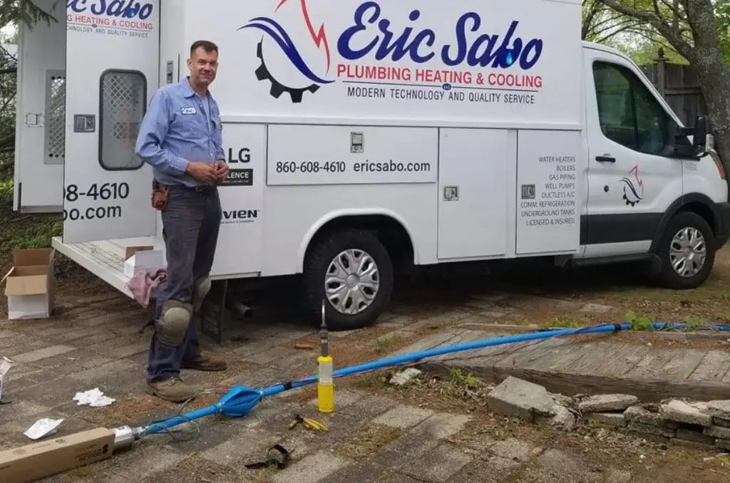 Plumber standing in front of a white Eric Sabo Plumbing, Heating & Cooling van